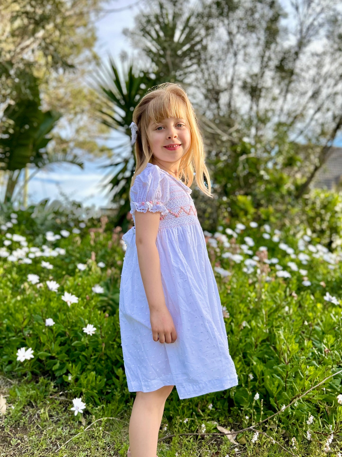 White dress for young girls featuring hand-stitched smocking and flutter sleeve